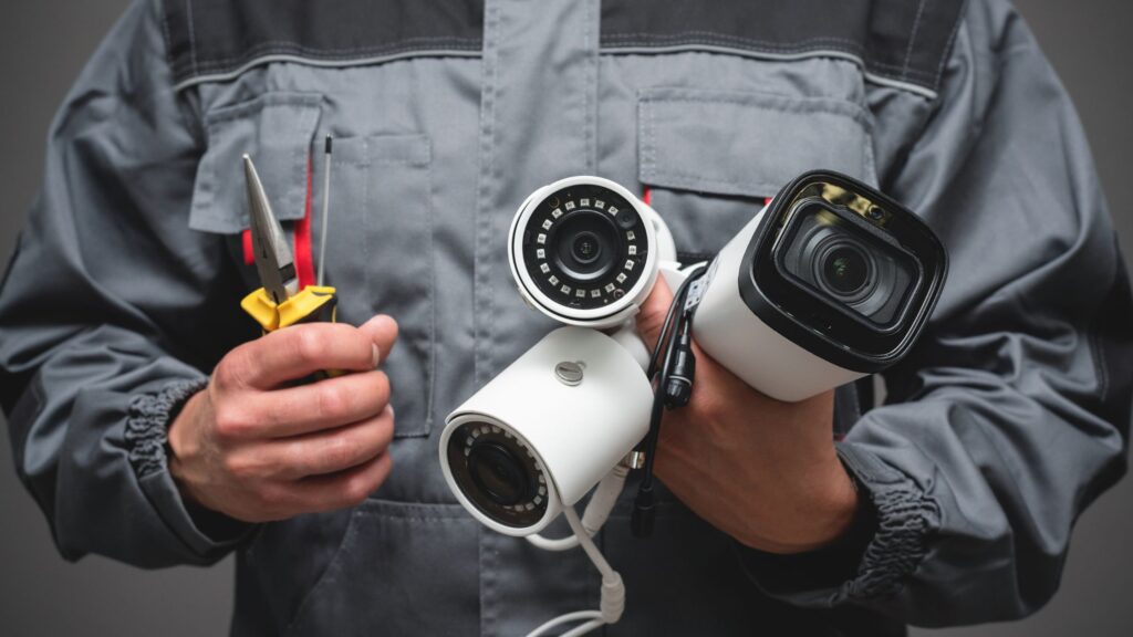 Technician holding security cameras and installation tools.