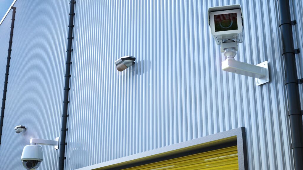 Industrial warehouse exterior with multiple mounted security cameras.